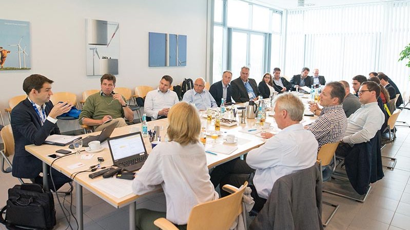 Mehrere Menschen sitzen an einem großen Tisch und besprechen Themen.