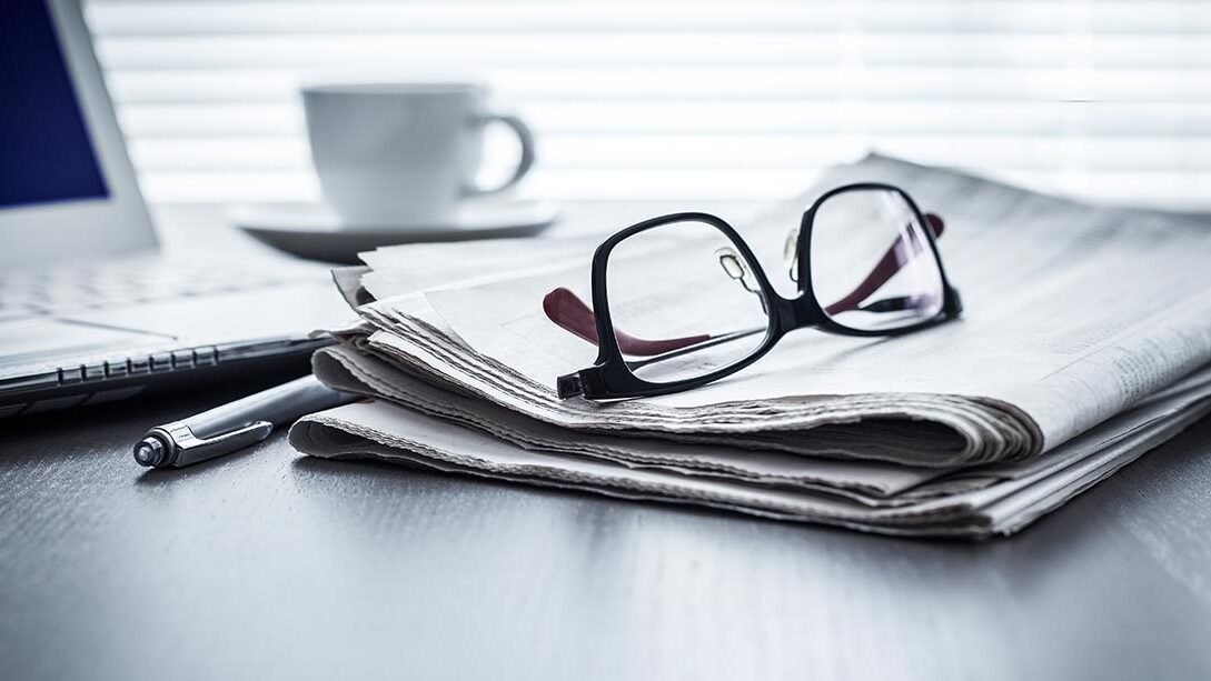 Nahaufnahme einer Zeitung auf der eine Brille liegt.